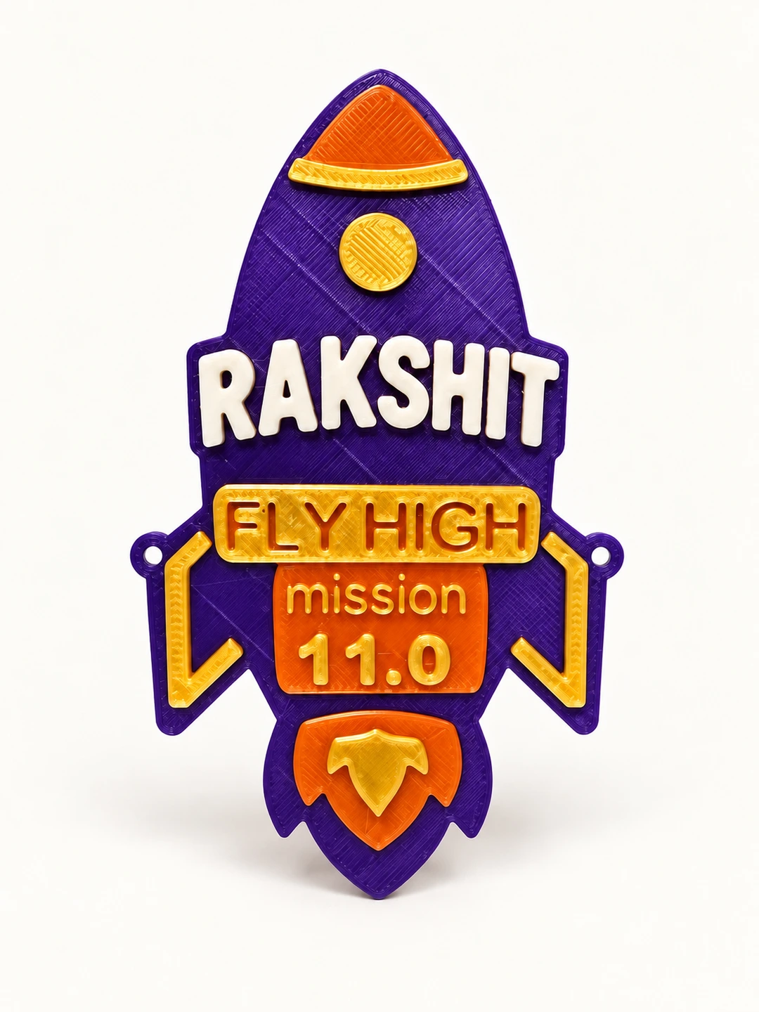 Purple, orange and gold 3D printed Inspiring Rocket fridge magnet with two purple side attachment rings, sample name Rakshit and age 11.0 on a clean background