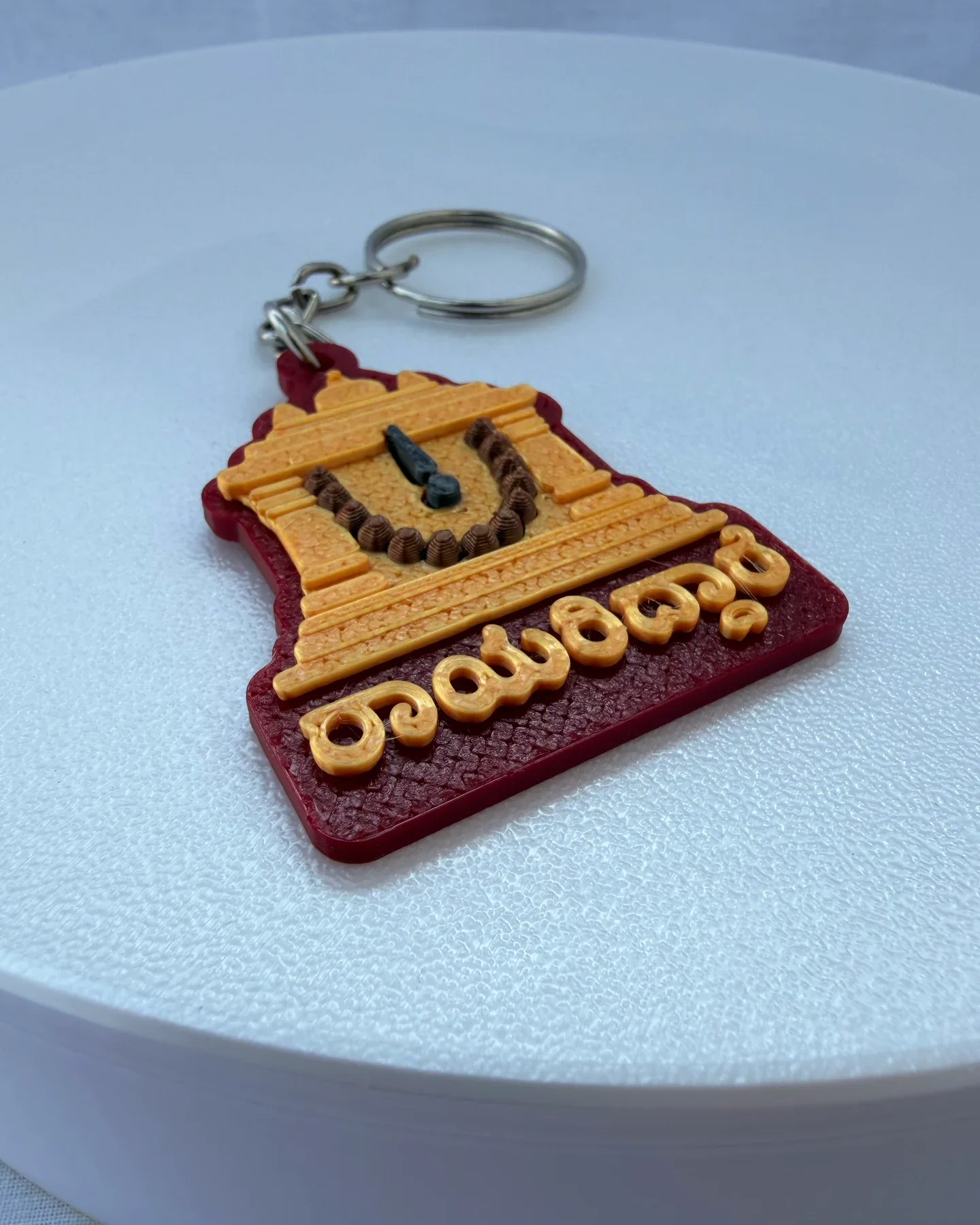 Close-up of the raised shrine, brown printed bead garland, dark nama mark and Kannada Rayariddare lettering on the burgundy charm