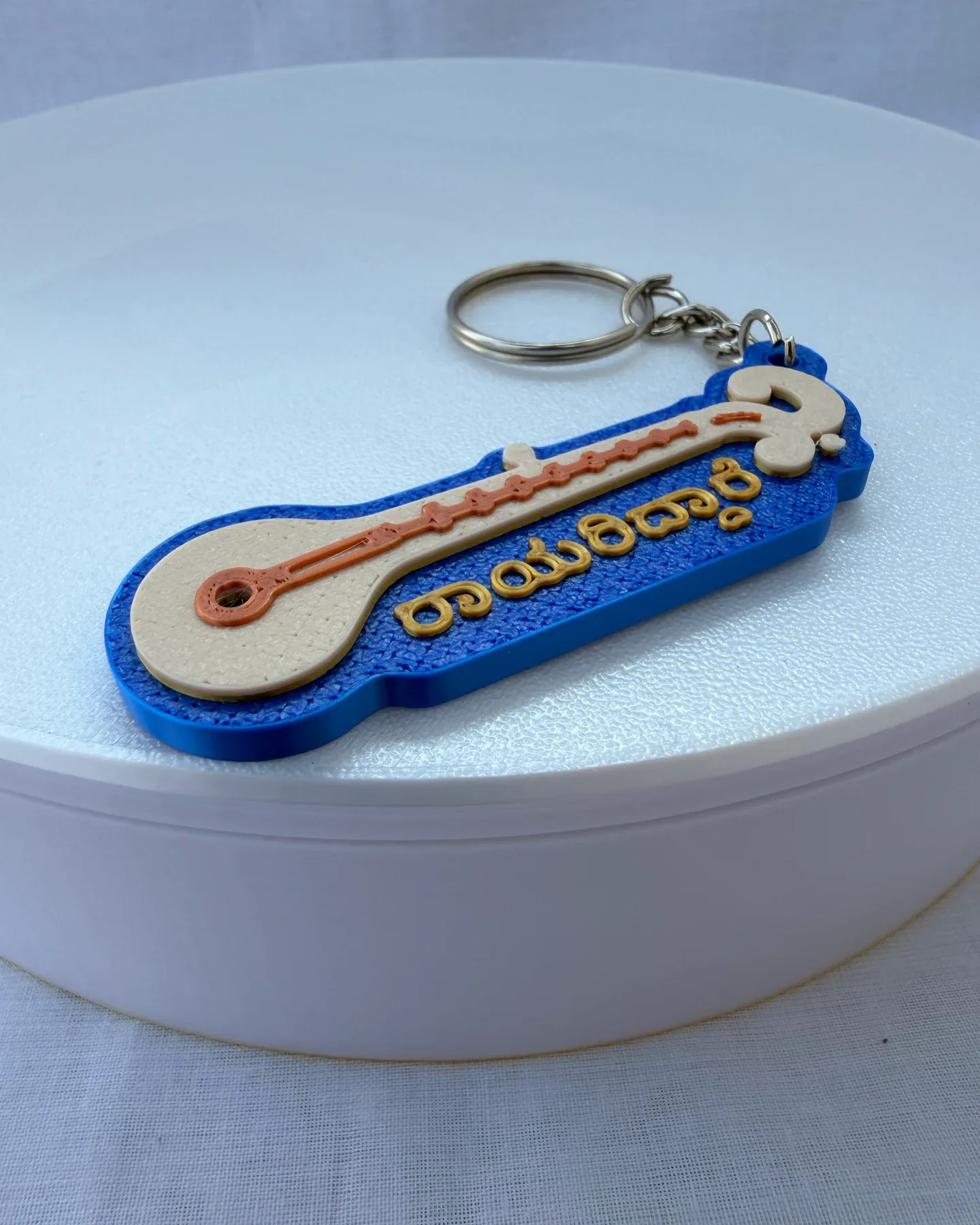 Close-up of the cream veena, orange details and raised gold-coloured Kannada lettering on the blue charm
